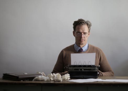 A thoughtful male writer typing on a vintage typewriter, surrounded by crumpled papers.
