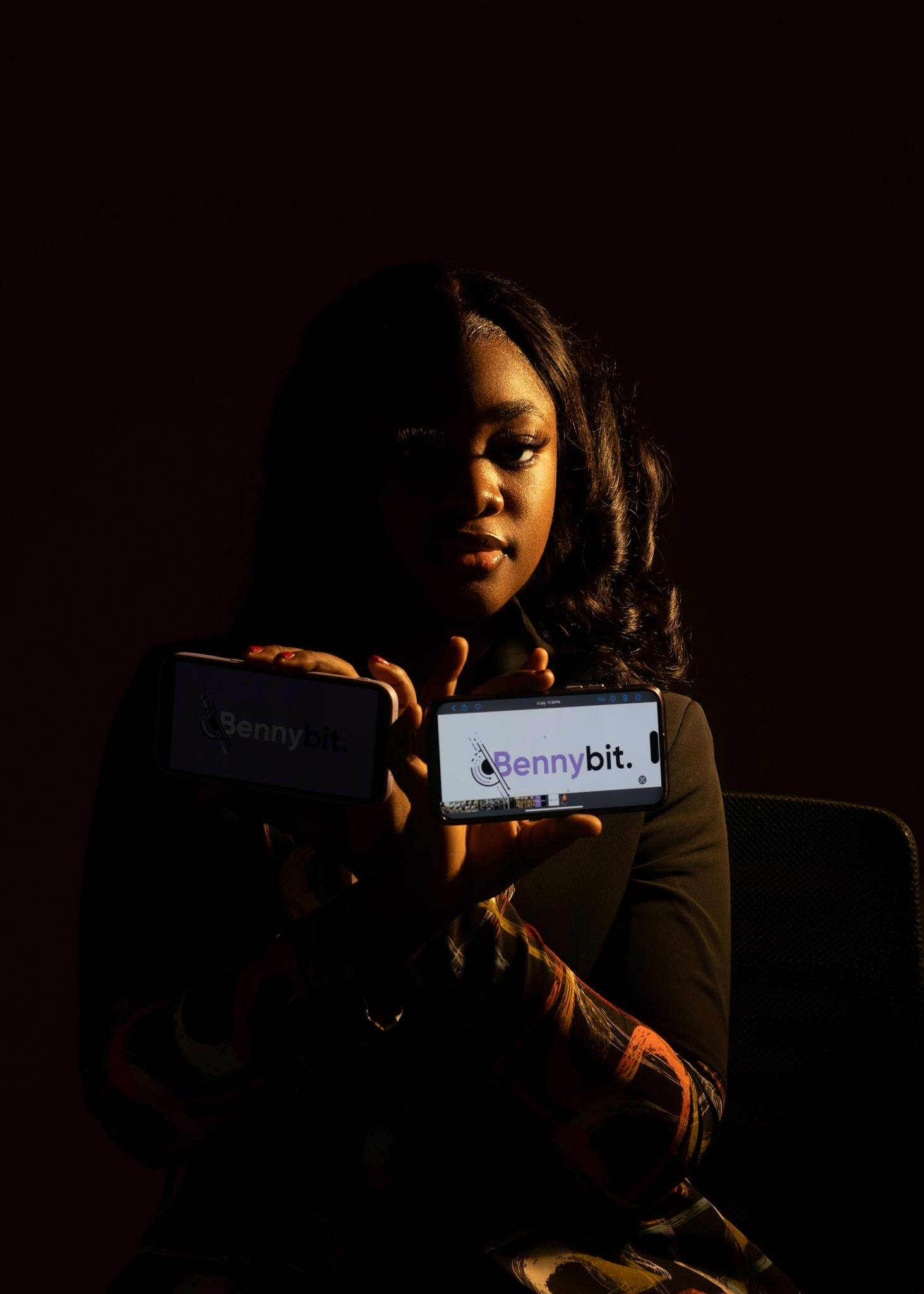 Portrait of a woman holding two phones displaying the Bennybit app in low light.